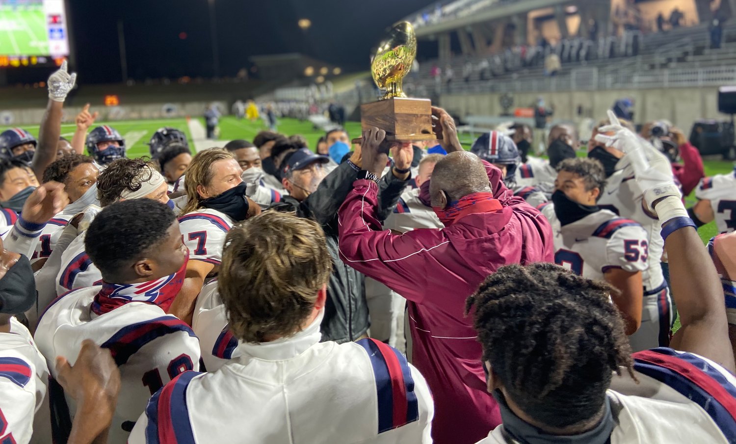 Tompkins head coach Todd McVey, in grey, hands off the district championship trophy to school namesake O.D. Tompkins, in crimson red, following the Falcons' win over Seven Lakes on Nov. 27.